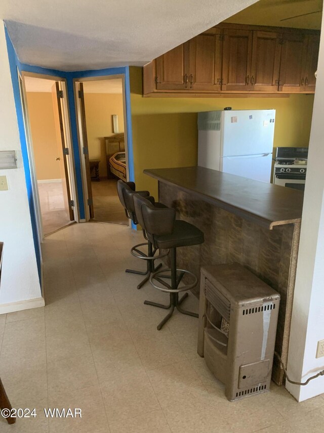 kitchen with a breakfast bar, dark countertops, white appliances, and brown cabinets