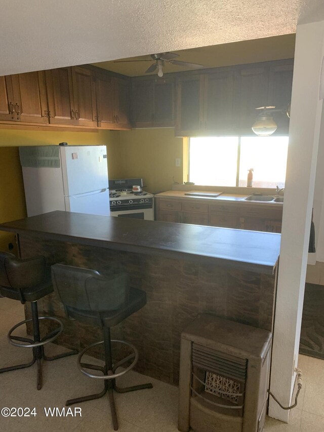 kitchen featuring brown cabinets, ceiling fan, white appliances, a peninsula, and a kitchen breakfast bar