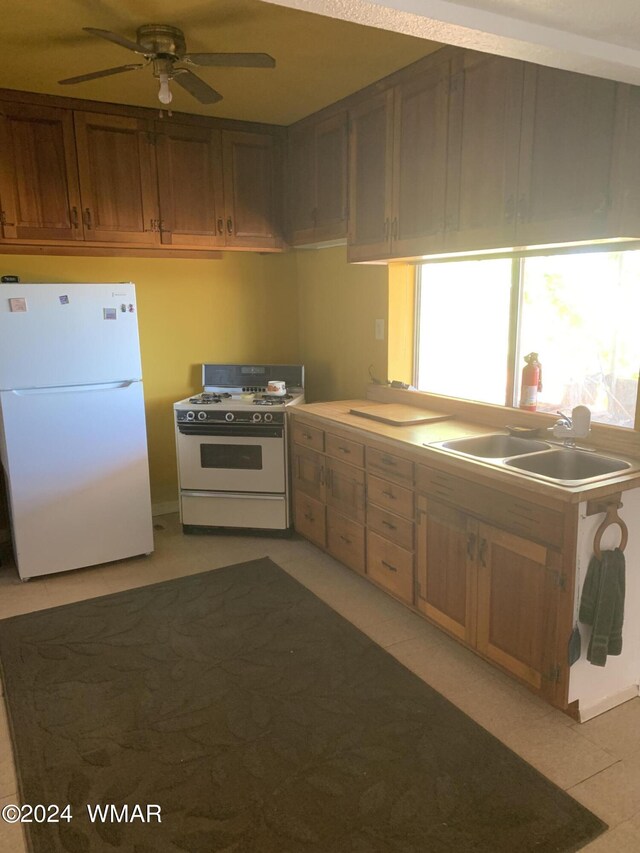 kitchen with light countertops, brown cabinetry, a ceiling fan, a sink, and white appliances