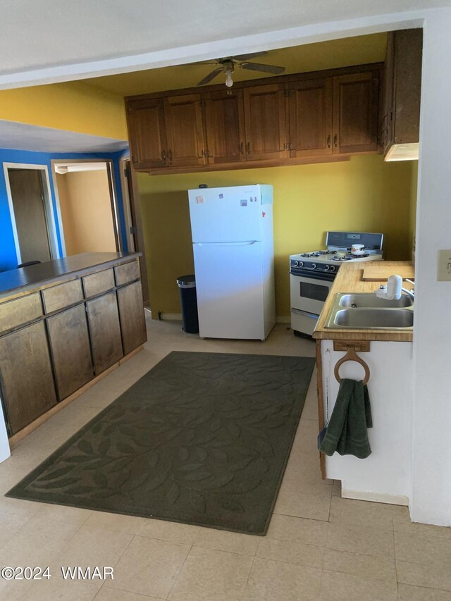 kitchen featuring ceiling fan, dark brown cabinetry, white appliances, a sink, and light countertops