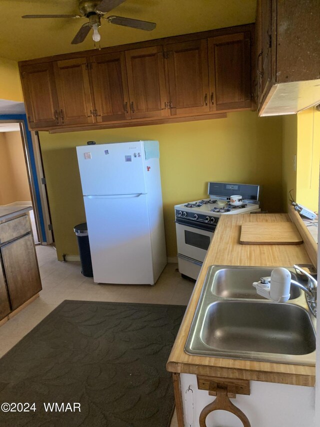 kitchen featuring brown cabinets, wooden counters, ceiling fan, a sink, and white appliances