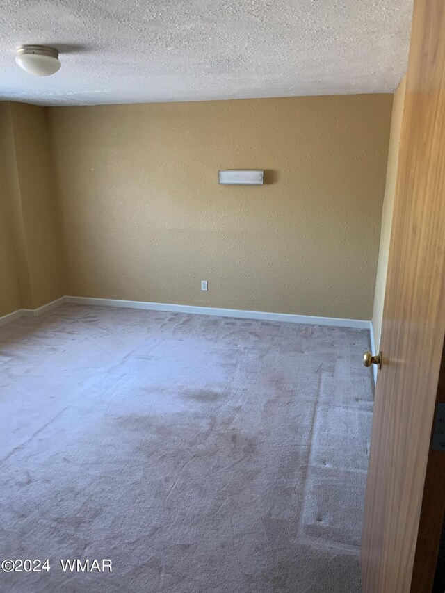 carpeted spare room featuring baseboards, a textured ceiling, and a textured wall