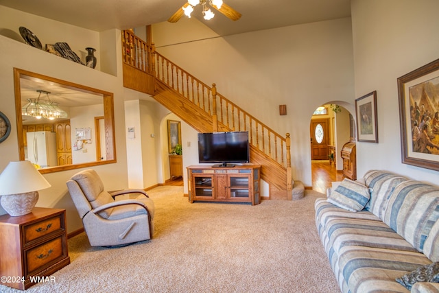 living area with light carpet, arched walkways, a ceiling fan, a towering ceiling, and stairway