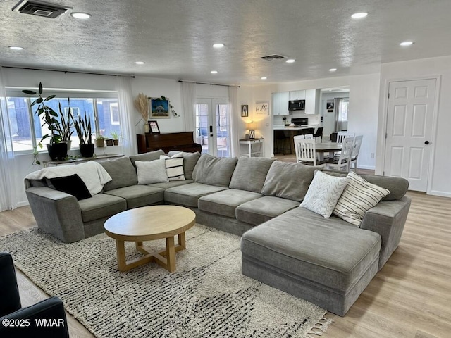 living area with a healthy amount of sunlight, light wood-style floors, visible vents, and french doors