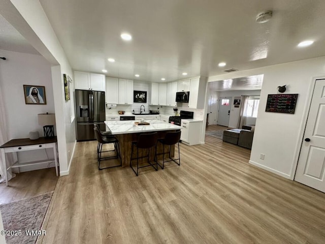 kitchen featuring light wood finished floors, white cabinets, a kitchen island, black range with gas stovetop, and stainless steel refrigerator with ice dispenser