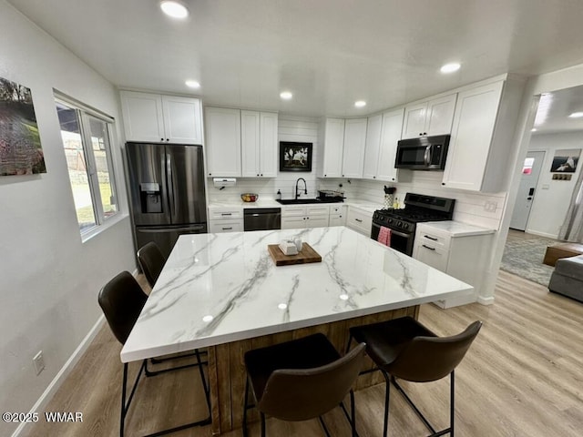 kitchen featuring black appliances, light stone counters, a kitchen bar, and white cabinetry