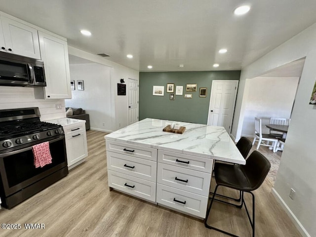 kitchen featuring gas range, stainless steel microwave, light stone counters, a center island, and white cabinetry