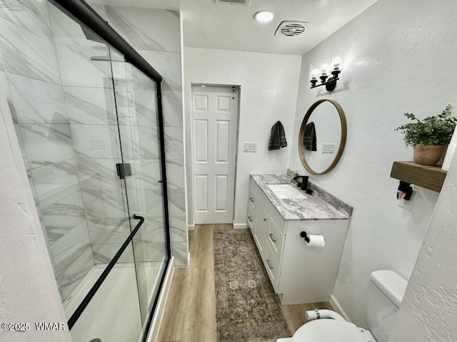 full bathroom featuring toilet, wood finished floors, vanity, visible vents, and a marble finish shower