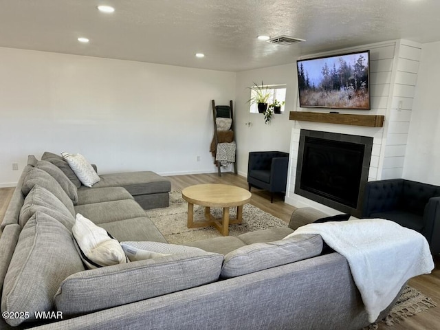 living area featuring a large fireplace, light wood-type flooring, visible vents, and recessed lighting