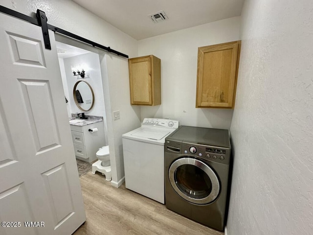 washroom with a barn door, visible vents, light wood-style floors, washer and dryer, and cabinet space