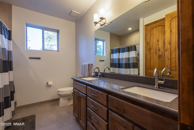 bathroom with double vanity, toilet, baseboards, and a sink