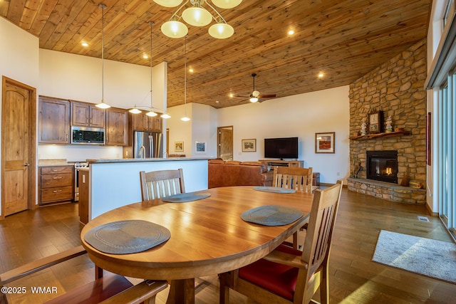 dining space with dark wood-type flooring, ceiling fan, wood ceiling, a fireplace, and a high ceiling