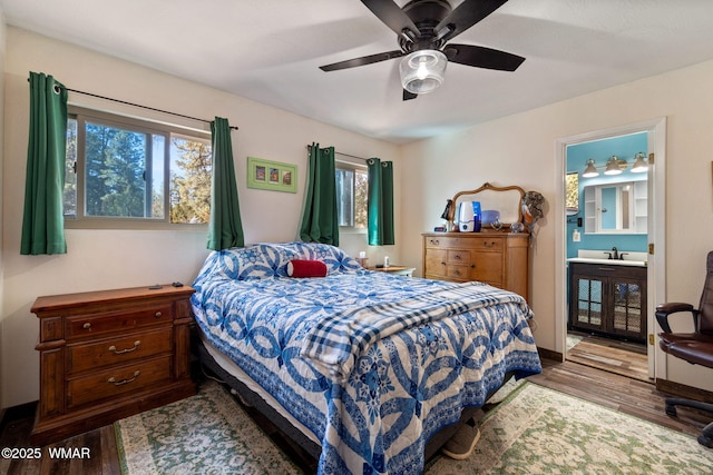 bedroom featuring connected bathroom, a sink, ceiling fan, wood finished floors, and baseboards