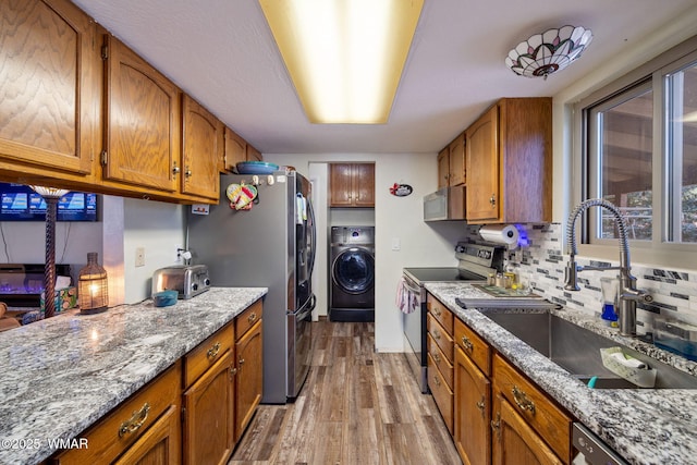 kitchen with stainless steel appliances, a sink, light wood-type flooring, washer / clothes dryer, and brown cabinetry