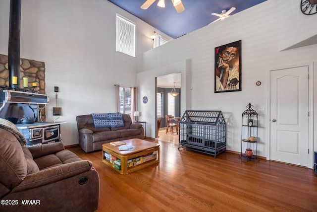 living room featuring baseboards, a ceiling fan, a wood stove, and wood finished floors
