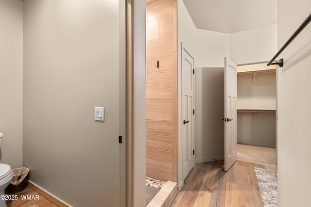 bathroom featuring toilet, hardwood / wood-style flooring, baseboards, and a tile shower