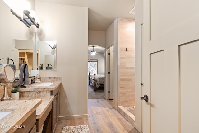 ensuite bathroom featuring connected bathroom, vanity, wood finished floors, tiled shower, and baseboards