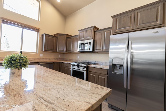 kitchen with light stone countertops, dark brown cabinetry, high vaulted ceiling, and stainless steel appliances