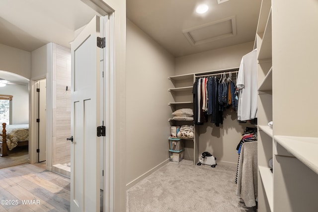 walk in closet with attic access, arched walkways, and light wood-style floors