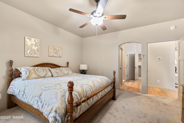 bedroom featuring a ceiling fan, arched walkways, light carpet, and light wood-style floors