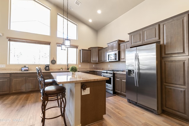 kitchen featuring visible vents, a kitchen island, appliances with stainless steel finishes, a breakfast bar, and light wood-type flooring