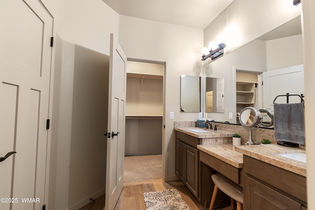 full bathroom featuring double vanity, baseboards, wood finished floors, a spacious closet, and a sink