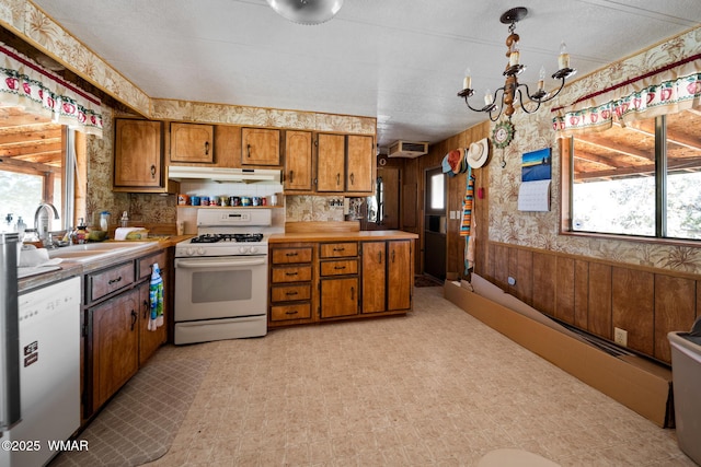 kitchen with light floors, brown cabinetry, a sink, white appliances, and under cabinet range hood