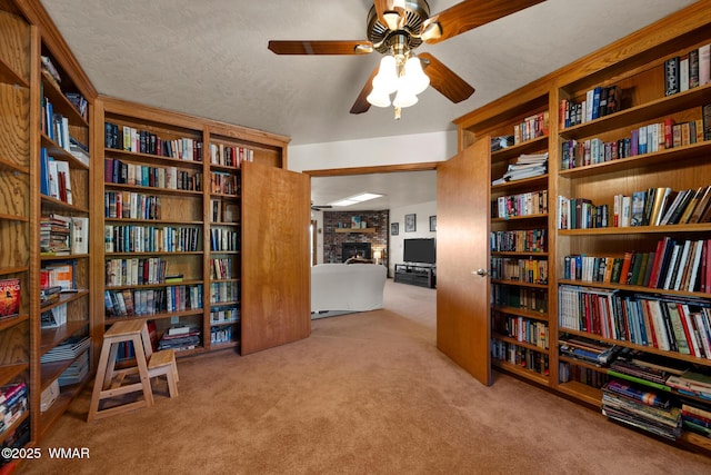 living area featuring carpet floors, wall of books, and a brick fireplace