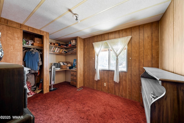 bedroom featuring a textured ceiling, wooden walls, carpet floors, visible vents, and a closet