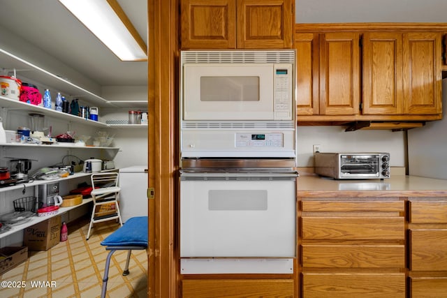 kitchen featuring white microwave, wall oven, a toaster, light countertops, and brown cabinets