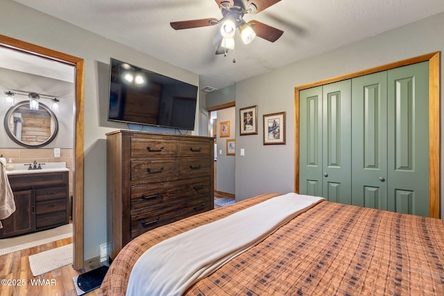 bedroom with a sink, a closet, a ceiling fan, wood finished floors, and ensuite bathroom