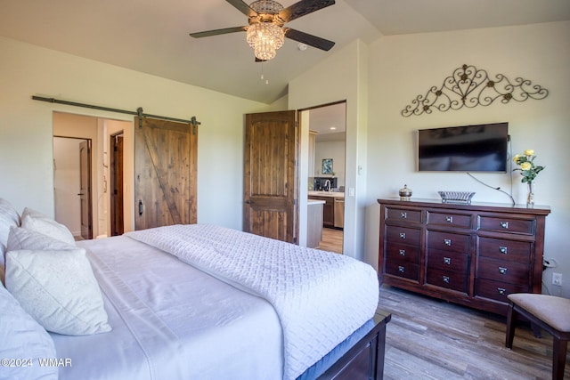 bedroom with lofted ceiling, a barn door, light wood-type flooring, and a ceiling fan