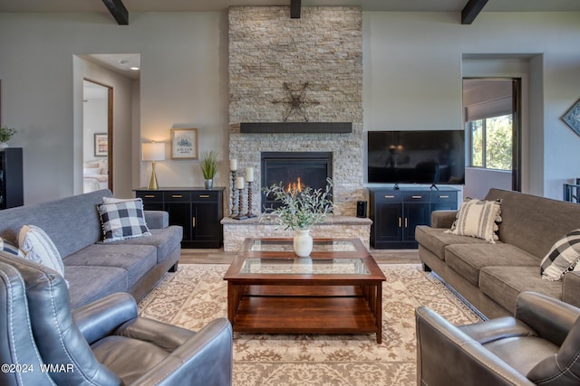 living room featuring light wood-style flooring, beamed ceiling, and a stone fireplace