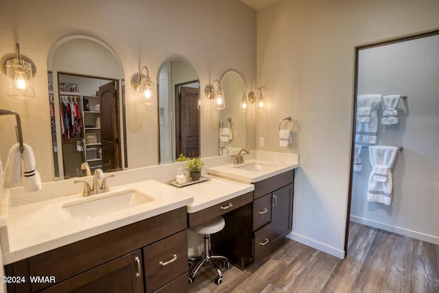 bathroom with double vanity, a walk in closet, a sink, and wood finished floors