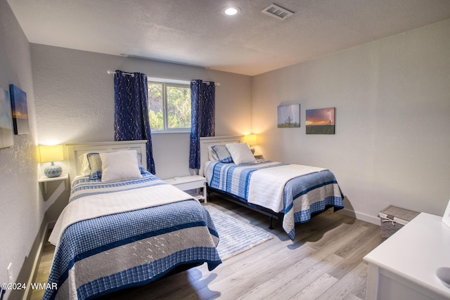 bedroom featuring baseboards, visible vents, a textured wall, a textured ceiling, and light wood-style floors