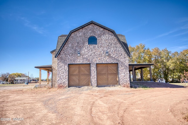 view of side of property with a garage, a gambrel roof, stone siding, and dirt driveway