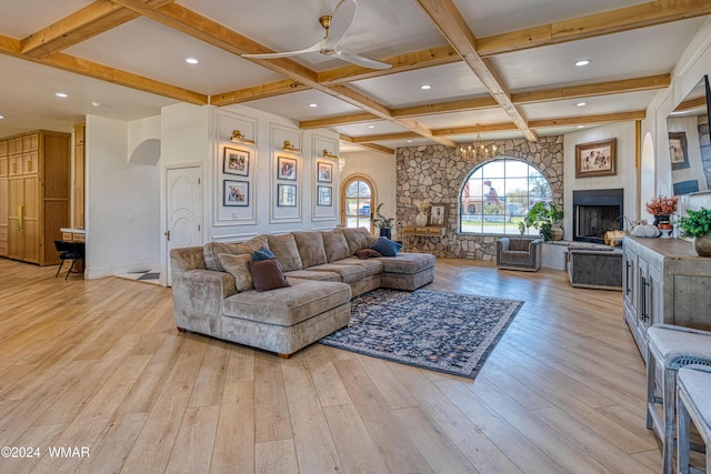 living room featuring a fireplace with raised hearth, light wood-style floors, coffered ceiling, beamed ceiling, and ceiling fan with notable chandelier