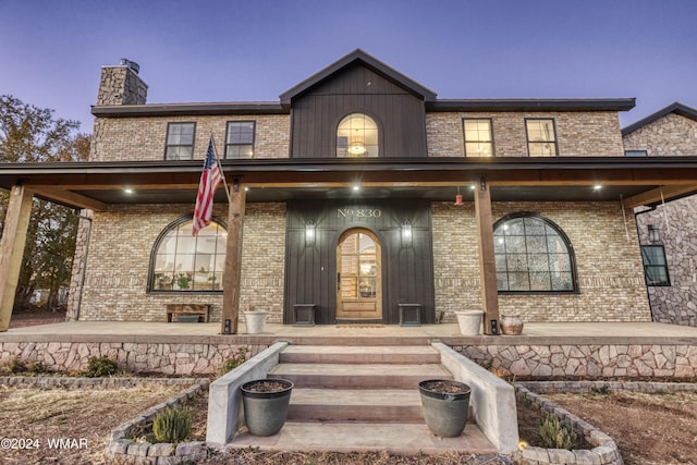 exterior entry at dusk with a chimney, a porch, and brick siding