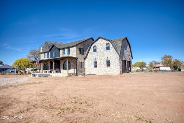 view of front facade featuring covered porch, stone siding, driveway, and a gambrel roof