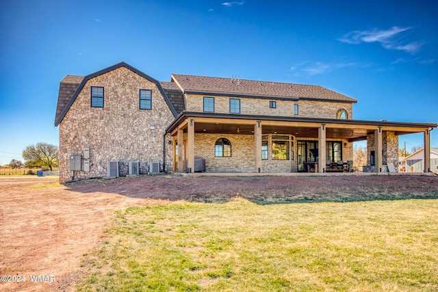 rear view of property with brick siding, a yard, central air condition unit, a gambrel roof, and a patio area