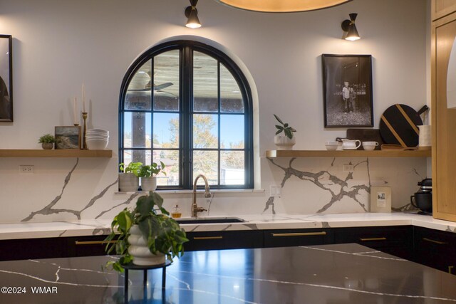 kitchen with decorative backsplash, dark cabinets, a sink, and light stone countertops