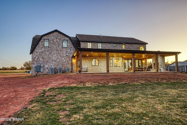 back of house at dusk with a lawn, central AC unit, a patio, and a gambrel roof