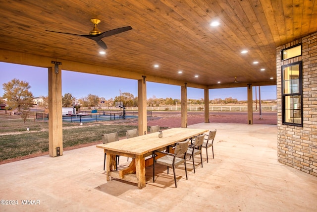 patio terrace at dusk with outdoor dining area, ceiling fan, and fence