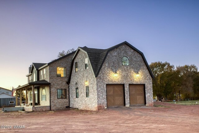 view of front of house with covered porch, driveway, a gambrel roof, and a garage