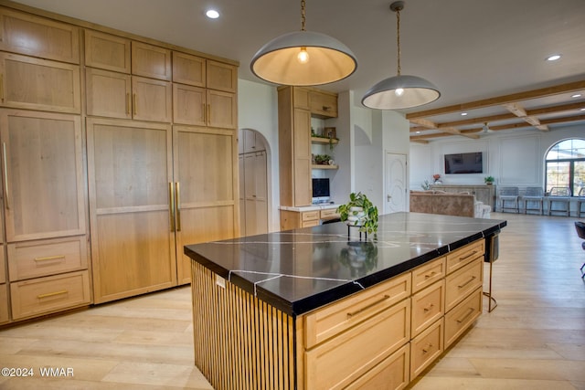 kitchen featuring light brown cabinets, light wood-style flooring, open shelves, dark countertops, and decorative light fixtures