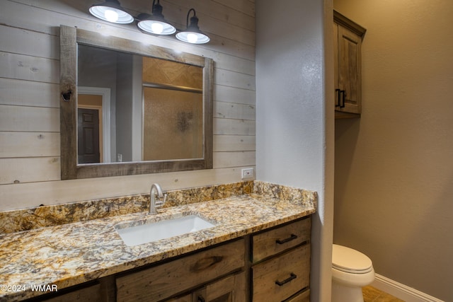 bathroom featuring toilet, wood walls, vanity, baseboards, and a shower stall