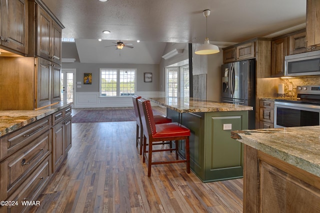 kitchen featuring brown cabinets, a breakfast bar area, stainless steel appliances, wainscoting, and a kitchen island