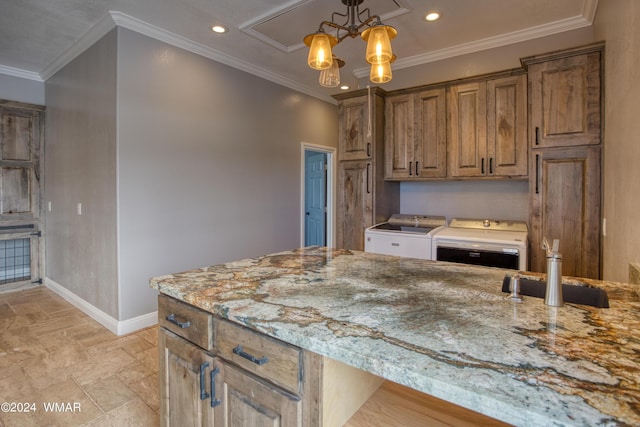 kitchen featuring light stone counters, a sink, baseboards, brown cabinetry, and washing machine and clothes dryer