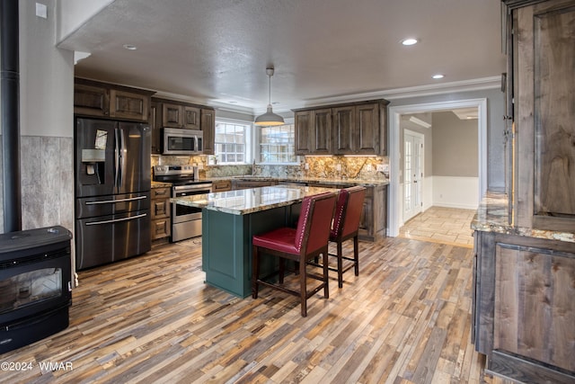 kitchen featuring light stone counters, stainless steel appliances, a kitchen island, dark brown cabinets, and a wood stove