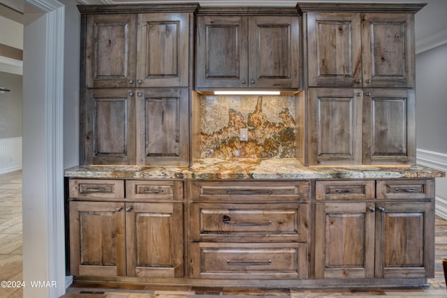 kitchen with light stone counters, ornamental molding, backsplash, and dark brown cabinets